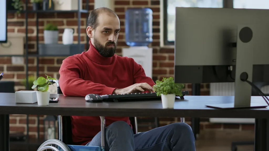 Uomo in sedia a rotelle lavora al computer in un ufficio accessibile