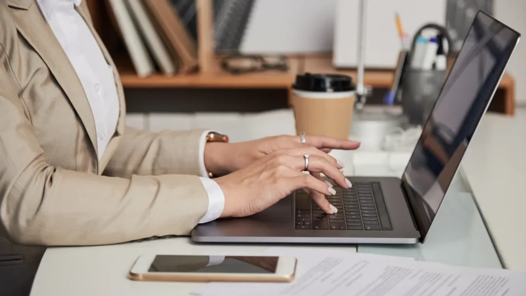 Mani di una donna che scrive al portatile in ufficio, senza volto visibile