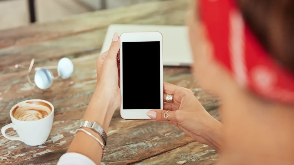Mani di una donna che tengono uno smartphone accanto a una tazza di caffè su un tavolo di legno