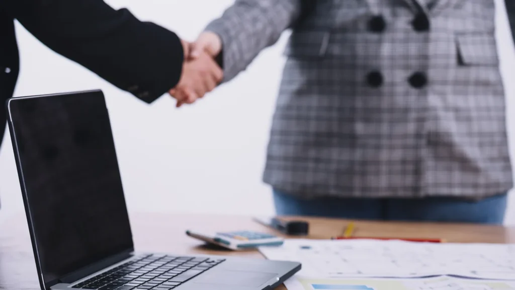 Stretta di mano tra due professionisti accanto a un portatile in ufficio